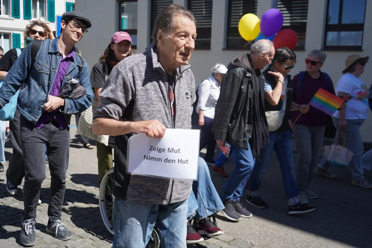 Man sieht ein Mann an einer Demo mit einem Schild. Darauf steht: Zeige Mut, nimm den Hut.